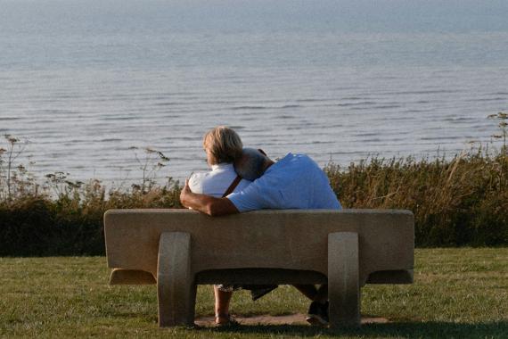 Ein Paar auf einer Bank am See. Der Mann lehnt an Schulter der Frau.